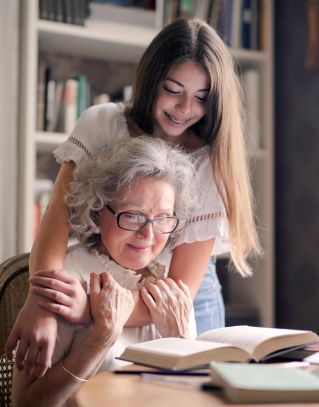 A heartwarming moment of a granddaughter embracing her grandmother as she reads a book together indoors.