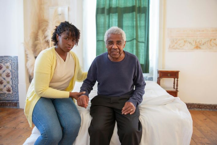 Daughter supporting elderly father in a bright, cozy room filled with love and warmth.