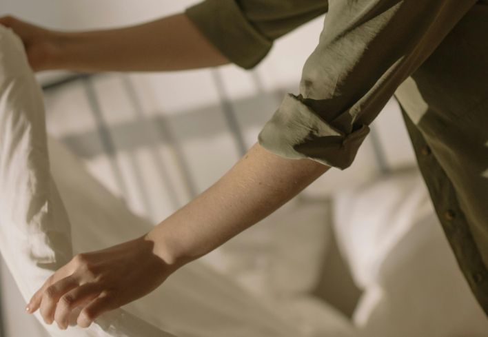 A person arranges fresh bed linen on a cozy bed in a warm, inviting bedroom setting.